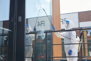 Side view portrait of male worker wearing protective suit spraying chemicals over building outdoors during disinfection, copy space