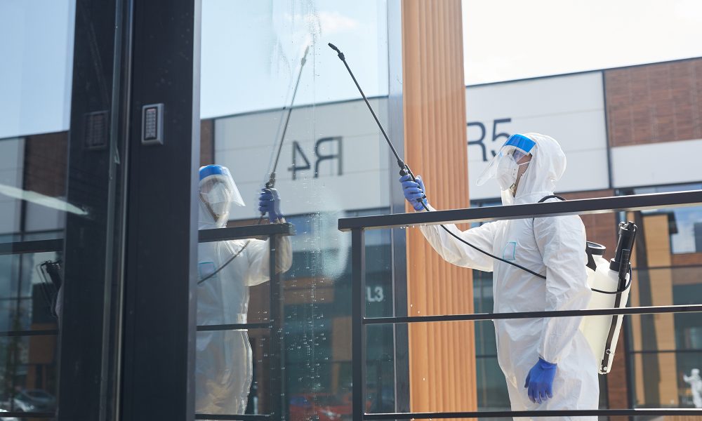 Side view portrait of male worker wearing protective suit spraying chemicals over building outdoors during disinfection, copy space